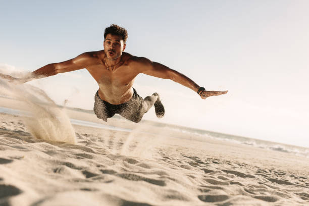 Man doing fitness workout at a beach on a sunny day. Bare chested athletic man jumping in air horizontally on beach while doing workout.