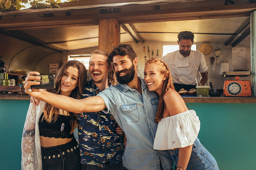 Happy millennial friends group taking selfie. Group of happy young people taking selfie with smartphone near a food truck.