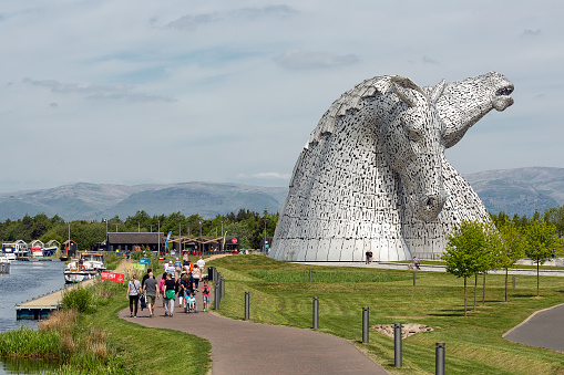 Falkirk, Scotland - May 19, 2018: People walking around horse structures Kelpies, famous sculptures of horse heads, public art by Andy Scott in Helix park near Falkirk