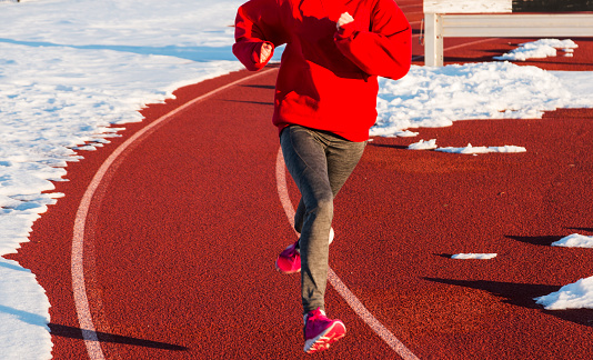 A high school runner is running on a red track surrounded by snow.