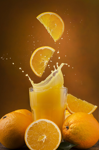 slices of orange fall into a glass filled with fresh juice generating a spray