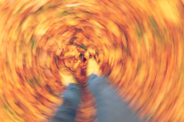 Motion blurred photograph of man or woman's feet walking through golden Fall or Autumn leaves stock photo