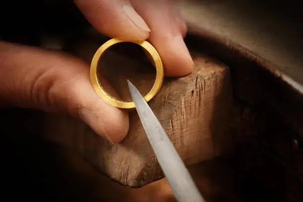 goldsmith hand holds a golden ring and works on it with a metal file, close up with copy space,  focus, narrow depth of field