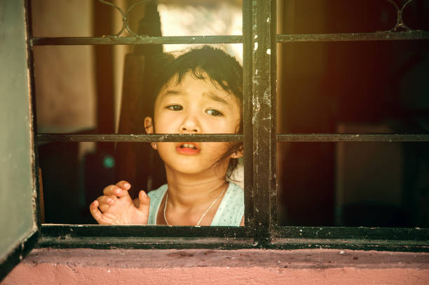 A sad looking girl out of the window waiting for someone or asking for help.