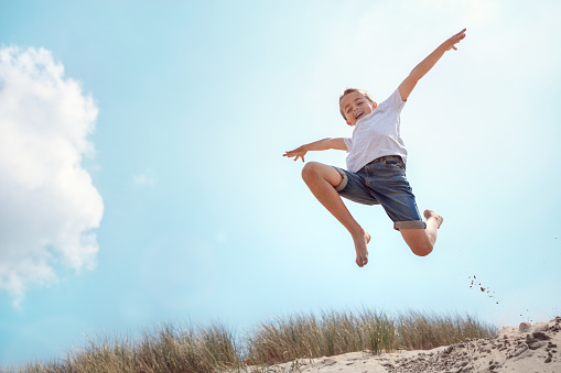 Boy leaping and jumping over sand dune on beach vacation