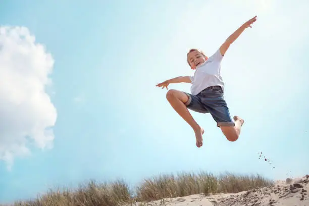 Photo of Boy running and jumping over sand dune on beach vacation