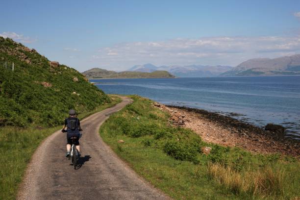 Sunart, Argyll & Bute, Scotland - May 28, 2018: A cyclist is on the single track road that follows the western shore of Loch Linnhe on the west coast of Scotland. In the distance is the Nevis range of mountains, which includes Ben Nevis, the highest mountain in the UK.