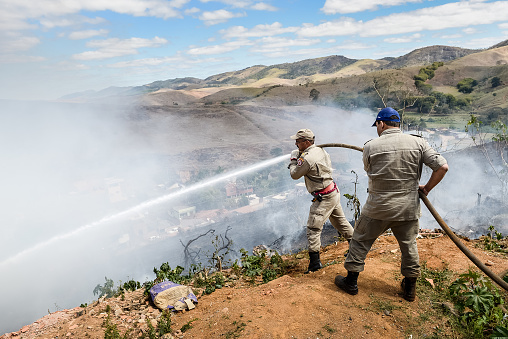 Valença (Rio de Janeiro), Brazil - June 09, 2014:  Firefighters are seen extinguishing a fire in a hill in Valença, south of Rio de Janeiro State. In Brazil, the Military Firefighters Corps (Corpo de Bombeiros Militar) is a military organization with the mission of civil defense, firefighting, and search and rescue inside the States of the Federation.