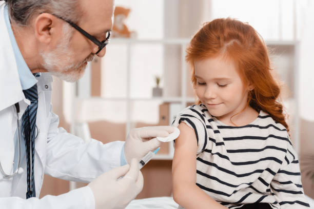 doctor in medical gloves making injection to little girl in clinic - senior adult hospital uniform gray hair imagens e fotografias de stock