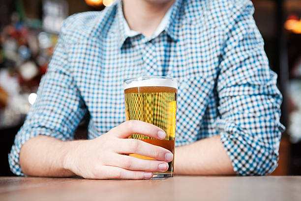 young man in bar, mid section - เบียร์ เครื่องดื่มแอลกอฮอล์ ภาพสต็อก ภาพถ่ายและรูปภาพปลอดค่าลิขสิทธิ์