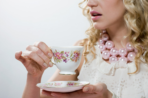 Cut out shot of unrecognizable woman standing over a table in the back yard and picking up the tea cup to serve to her husband for afternoon tea.