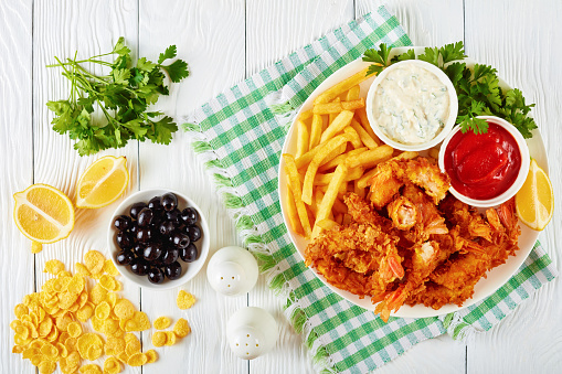 corn flakes breaded deep-fried crispy shrimps on a plate on wooden table, horizontal view from above, flat lay