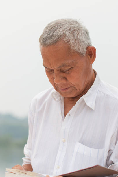 istock Adult education Learning Studying concept : Happy Asian Elderly man sitting reading book at riverside outdoor for learning or relax by self 977631182