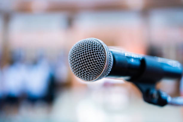 istock Microphones on abstract blurred of speech in seminar room, speaking conference hall light for presentation in exhibition event Background. Mic is transducer that convert sound into electrical signal. 977643692
