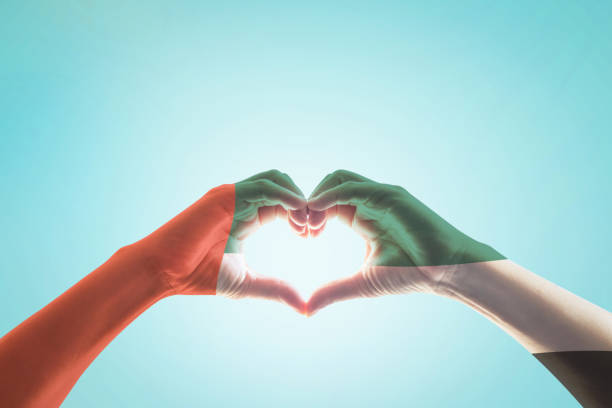 istock UAE, United Arab Emirate national flag pattern on people's hands in heart shape on blue mint sky background 977683420