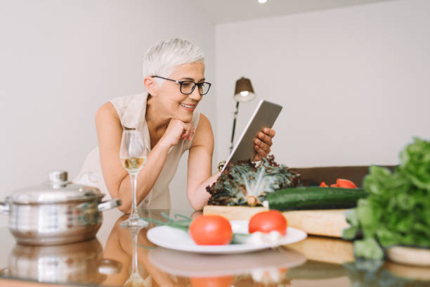 istock Happy woman leaning on kitchen table with vegetables on it and looking at digital tablet 977684128