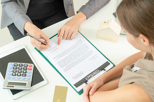 Client signs document regarding real estate activity next to lawyer or real estate agent sitting at office desk. Business concept of selling and buying house.