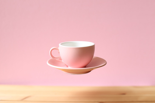 Pink empty coffee cup floating on wooden table