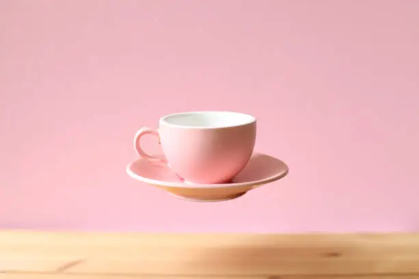 Photo of Pink empty coffee cup floating on wooden table
