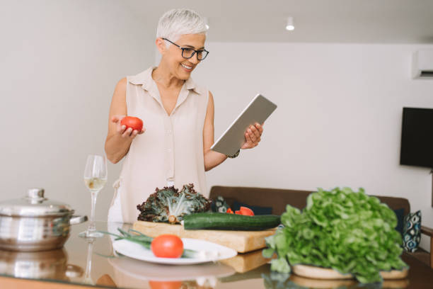 istock Happy woman smiling while holding tomato in one, and digital tablet in other hand 977687330