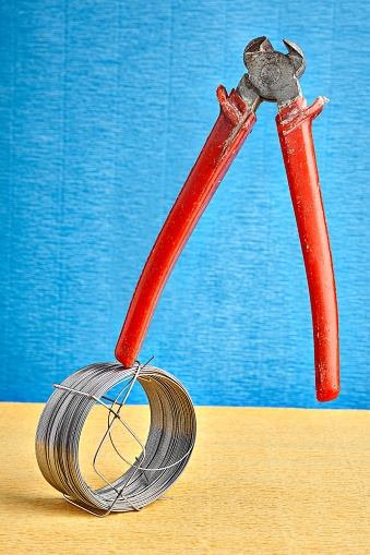 Old end cutting pliers are balanced standing upright on coil of steel wire, on blue background.