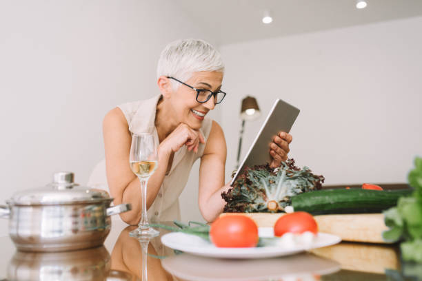 istock Mature woman leaning on kitchen table and reading from digital tablet with a smile on her face 977687874