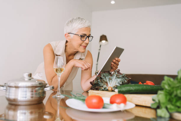 istock Elderly woman leaning on kitchen counter and looking at digital tablet 977691116