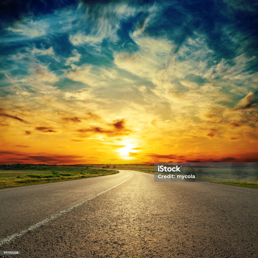 orange sunset in low dramatic clouds over asphalt road Sunset Stock Photo