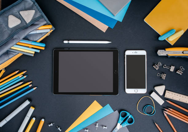 istock Top view of various school supplies on black background. Electronic learning concept. 977747328