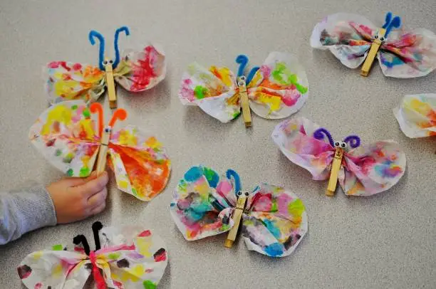 Funny and easy butterflies made from coffee filters, clothespins and chenille stems. ( Blurry child's hand holding and showing his project. )