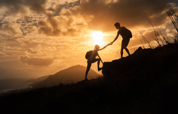 istock People helping each other hike up a mountain at sunrise. 977818074