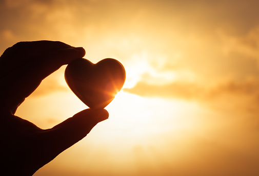 Hand holding heart against a golden sunset.