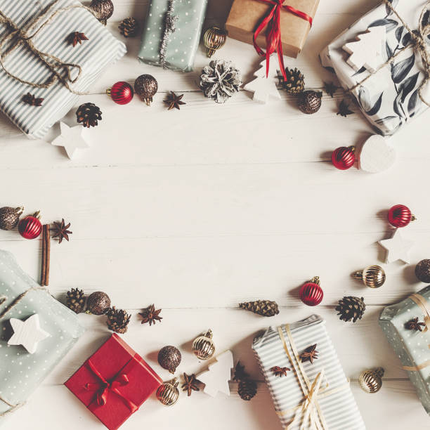 istock christmas flat lay mock up. present boxes with ornaments and pine cones anise on white wooden background top view, space for text. stylish wrapped gifts. seasonal greetings card. happy holidays 977844046