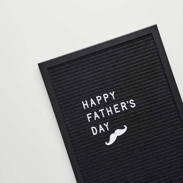 Black letterboard with white plastic letters with quote Happy Father's Day, on white background. Flat lay, square crop.