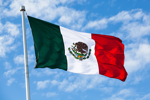 Flag of Mexico waving in the wind, over partly cloudy sky