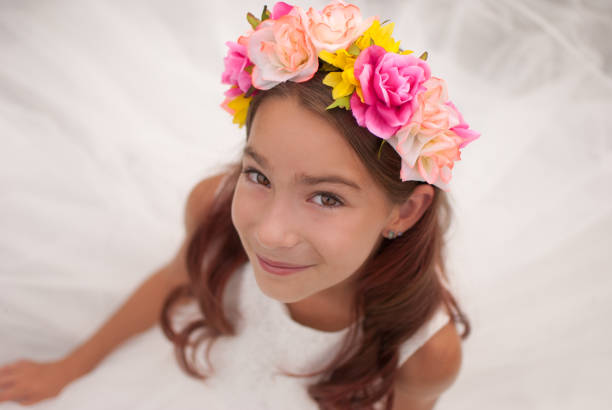 Girl with flower headband and white dress girl with brown hair and brown eyes wearing white dress and flower headband closeup looking at camera flower girl stock pictures, royalty-free photos & images