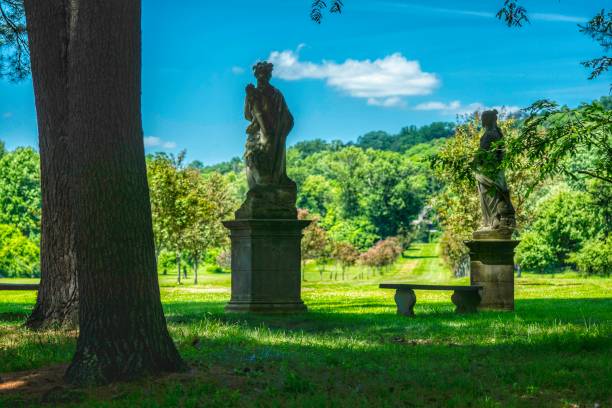 istock Two classical statues and a bench in a lush garden. 977965072