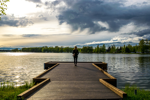 Lonely woman daydreaming, looking at Lake Spenard, Anchorage, with the beautiful sky at sunset