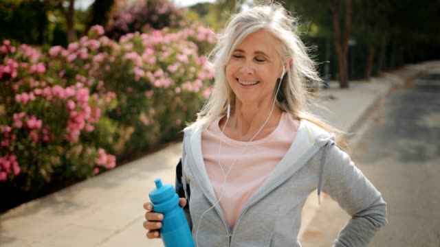 Mature woman taking a break from running outdoors and drinking water