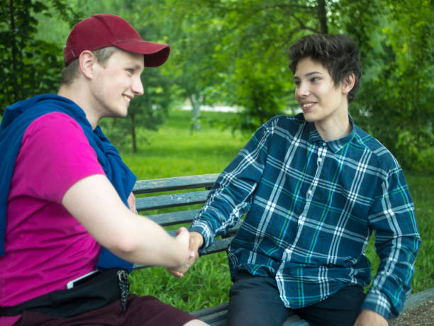 istock two young smiling friends handshake saluting each other sitting on the bench outdoors on a summer day 978179320