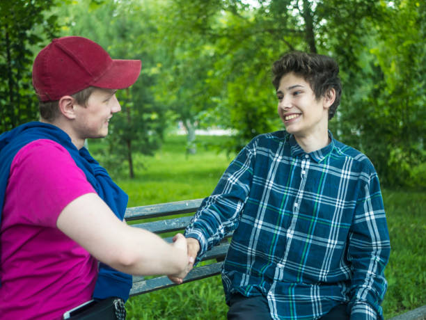 two young smiling and laughing brothers in casual clothes shake hands  outdoors on the bench