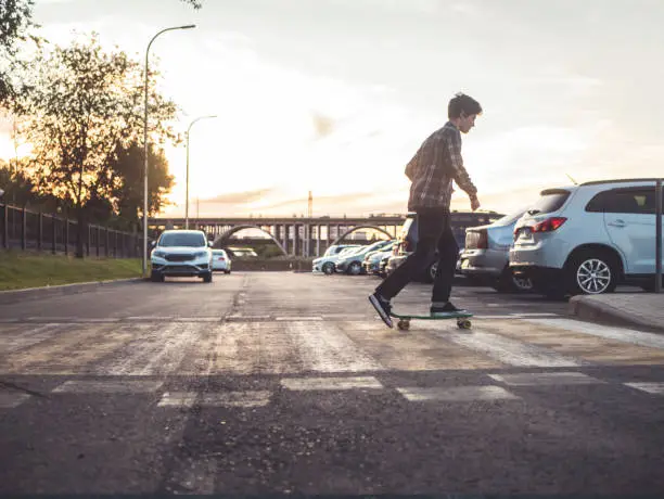 Photo of young hipster boy crossing the street riding the skateboard in the urban city