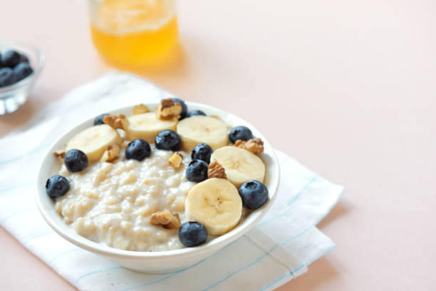 Oatmeal porridge with walnuts, blueberries and banana in bowl on pink pastel background - healthy organic breakfast, oats with fruits, honey and nuts