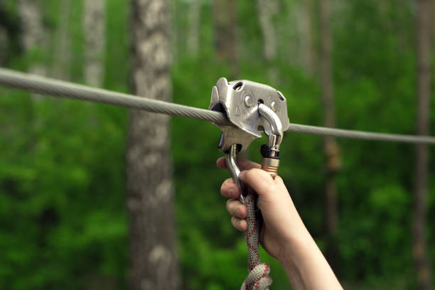 Hands holding carabiner on zip line Zip line activity. Hands holding carabiner on zip line in forest. metal clip stock pictures, royalty-free photos & images