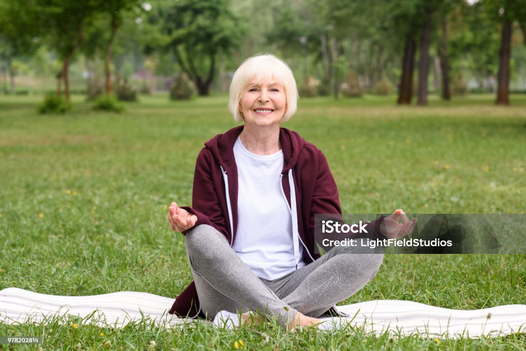 happy senior woman meditating with gyan mudra on yoga mat in park Active Lifestyle Stock Photo