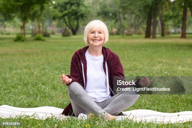 Happy Senior Woman Meditating With Gyan Mudra On Yoga Mat In Park Stock Photo - Download Image Now