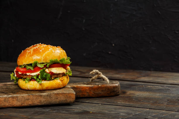 istock Hamburger on a wooden board against a dark background with copy space. Hamburger with sauce and fresh vegetables on a wooden table. Burger. 978216204