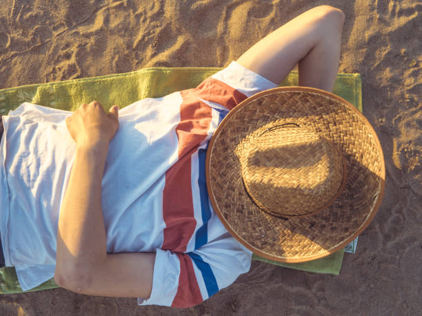 istock overhead view of man sleeping on the sand with hat on face 978258136