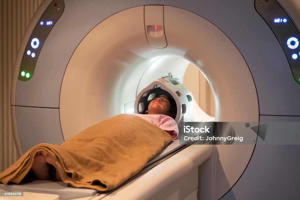 Asian girl on MRI scanner Young female patient laying straight, with blanket over her, inside tube of MRI scanner MRI Scan Stock Photo