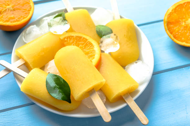 istock Orange popsicle on blue wooden background. Summer refreshing ice cream on stick. 978265556